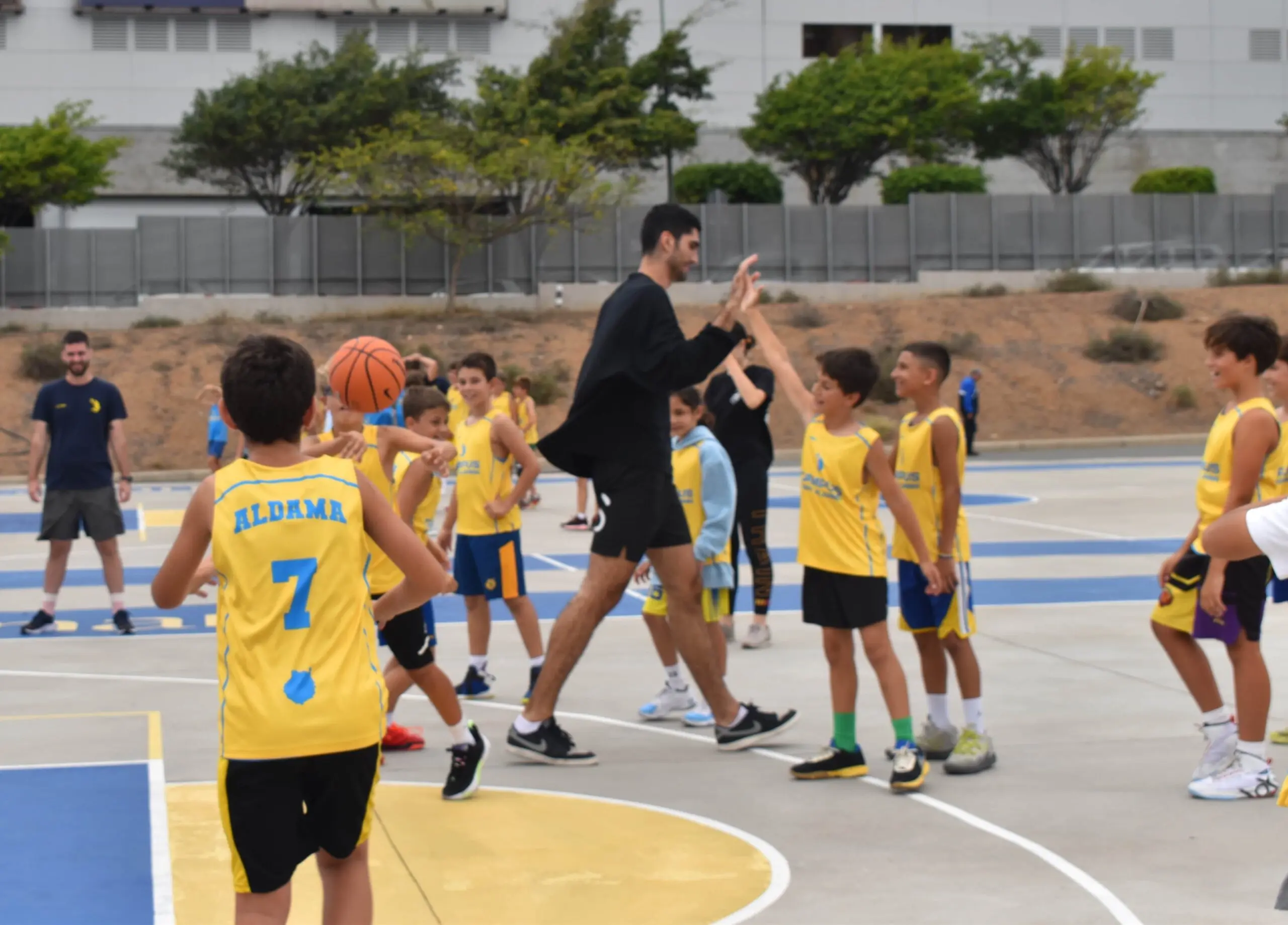 Santi Aldama saludando a participantes del campus de baloncesto en Gran Canaria durante una jornada de ejercicios en pista exterior